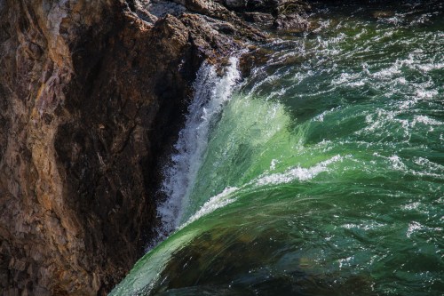 A close-up of a waterfall cascading over rocky cliffs into a vibrant green pool below.