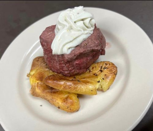 A plate featuring a tender beef filet topped with creamy sauce, served alongside roasted potatoes.