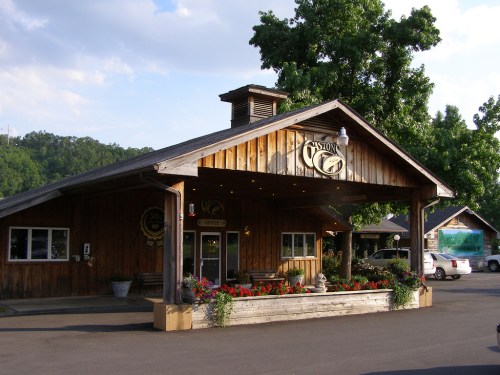A rustic wooden building with a sloped roof, surrounded by greenery and colorful flowers, serving as a welcoming entrance.