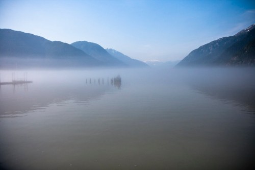 A serene lake surrounded by misty mountains, with reflections on the water and a calm, tranquil atmosphere.