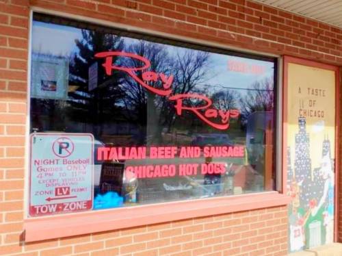 Window display of Ray Ray's featuring "Italian Beef and Sausage" and "Chicago Hot Dogs," with a nearby parking sign.