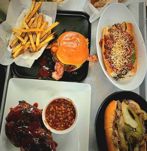 A spread of delicious food including fries, a burger, a hot dog with toppings, baked beans, and a meat sandwich.