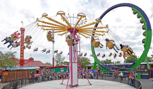 A vibrant amusement park scene featuring a swing ride and a large Ferris wheel, with excited riders and a crowd below.