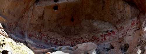 Ancient cave paintings on a rocky wall, featuring red and black figures and symbols in a natural cave setting.