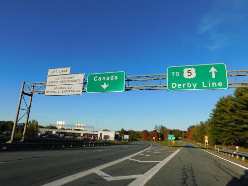 Road sign indicating the left lane for US Customs and directions to Canada and Derby Line. Clear blue sky above.