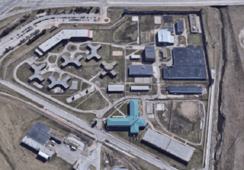 Aerial view of a large correctional facility with multiple buildings and outdoor areas, surrounded by open land.