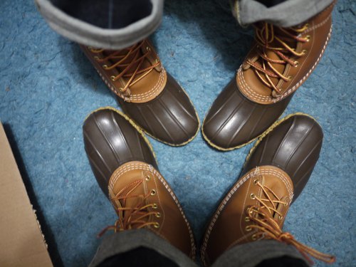 Two pairs of brown and tan boots on a blue carpet, with feet positioned in a circle.