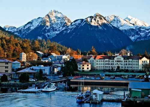 A scenic view of a harbor with boats, surrounded by mountains and a small town bathed in warm sunlight.