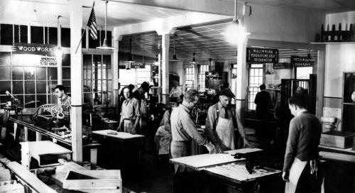 A black-and-white photo of a woodworking shop with several workers engaged in various tasks and machinery.
