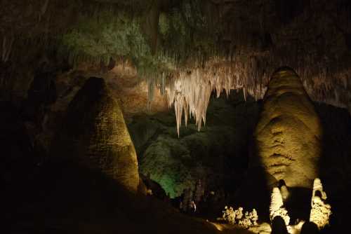 Stalactites and stalagmites in a dimly lit cave, showcasing unique rock formations and vibrant green hues.