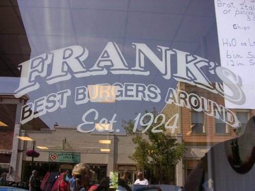 Sign for "Frank's Best Burgers Around" established in 1924, seen through a window with people outside.
