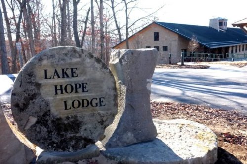 Sign for Lake Hope Lodge in a wooded area, with a stone structure in the foreground and a lodge building in the background.