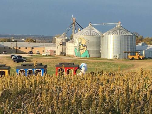 A colorful train in a field with silos and a large mural of a cartoon character in the background.