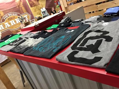 A display of various t-shirts in different colors and designs, arranged neatly on a red table in a market setting.