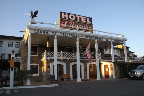 Historic hotel with a large sign, American flag, and a charming facade featuring white columns and stone details.