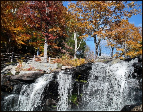 A scenic waterfall surrounded by vibrant autumn foliage and clear blue skies.