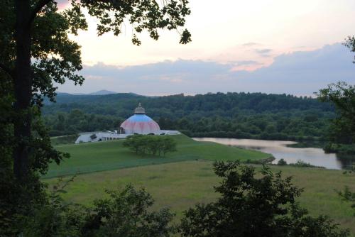 A serene landscape featuring a dome-shaped building by a lake, surrounded by lush greenery and distant hills at sunset.