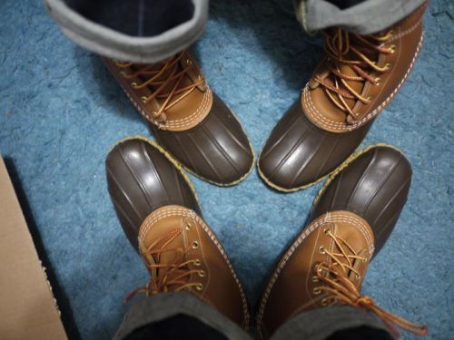 Two pairs of brown and tan winter boots on a blue carpet, with jeans visible above the boots.