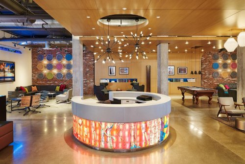 Modern office lobby with a circular reception desk, colorful decor, seating areas, and artistic lighting fixtures.