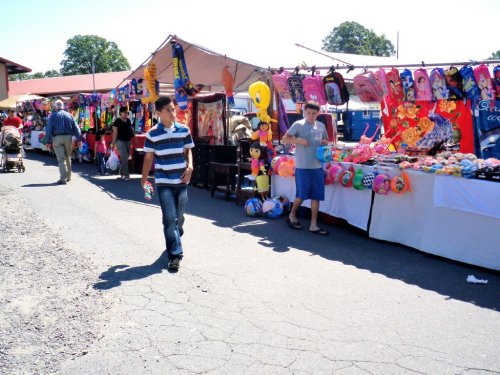 A bustling market scene with colorful stalls selling various goods, and people walking along the pathway.