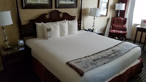 A cozy hotel room featuring a large bed with white pillows, a patterned throw, and elegant furnishings.