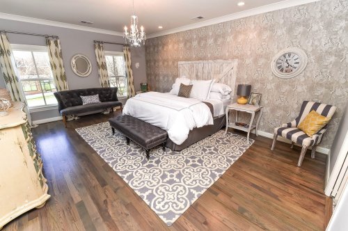 Cozy bedroom with a large bed, stylish decor, a patterned rug, and a mix of seating options. Natural light from windows.