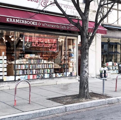 Exterior of Kramerbooks & Afterwords Cafe, featuring a large window displaying books and a tree in front.
