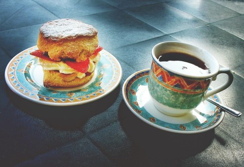 A plate with a strawberry shortcake beside a cup of black coffee on a patterned table.