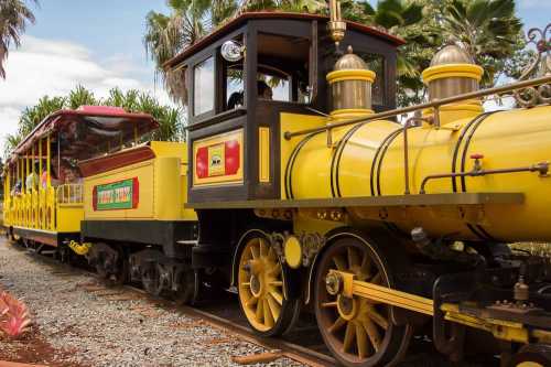 A colorful yellow train with a vintage design, parked on a track surrounded by lush greenery.