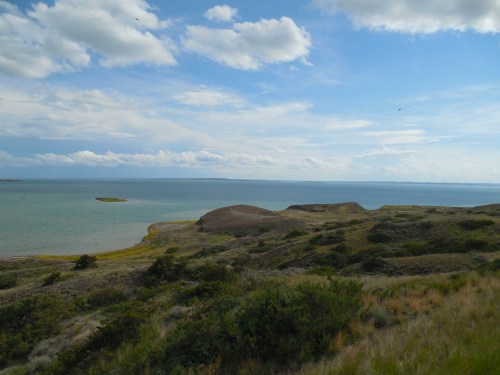 A scenic view of rolling hills meeting a calm sea under a partly cloudy sky.