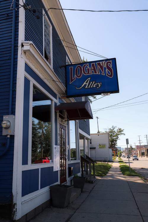 Exterior of Logant's Alley, a blue building with a prominent sign, featuring a sidewalk and nearby street view.