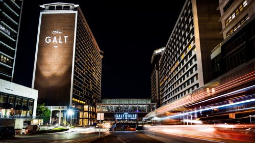 Night view of the Galt House hotel with illuminated signage and light trails from passing vehicles.