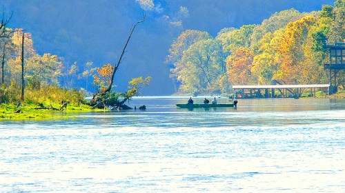 A serene river scene with autumn foliage, a small boat with people, and a dock in the background.