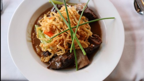 A plate of savory dish featuring tender meat, vegetables, and crispy fried onions, garnished with green onions.
