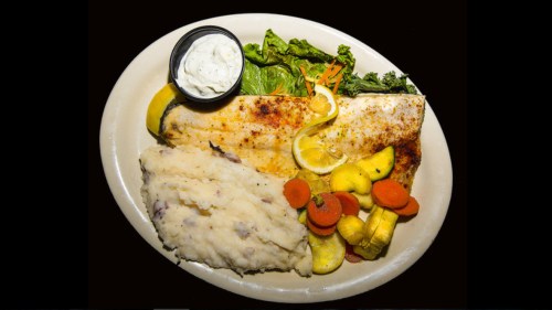 A plate featuring grilled fish, mashed potatoes, sautéed vegetables, and a side of dipping sauce.