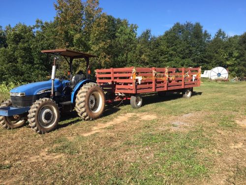 A blue tractor with a red trailer parked on a grassy field, surrounded by trees and a clear blue sky.