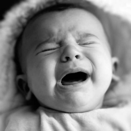A close-up of a crying baby with a distressed expression, captured in black and white.