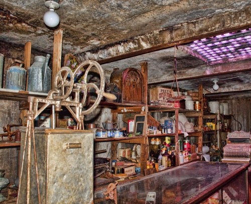 A cluttered vintage shop interior filled with old tools, jars, and various antiques on wooden shelves.