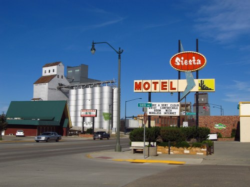 A roadside view featuring the Siesta Motel sign, grain silos, and a clear blue sky.