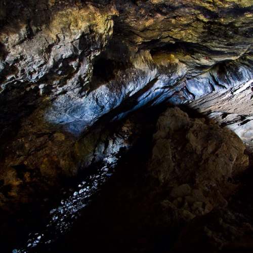 A dimly lit cave interior with rocky walls and a small stream of light illuminating the ground.