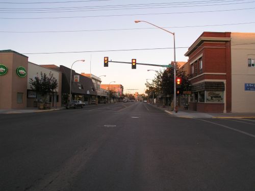 Empty street view at dusk, featuring storefronts and a traffic light showing red.