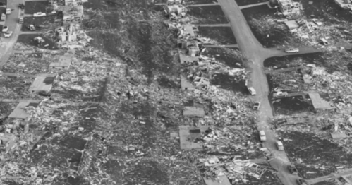 Aerial view of a devastated area, showing debris and damaged structures after a disaster.