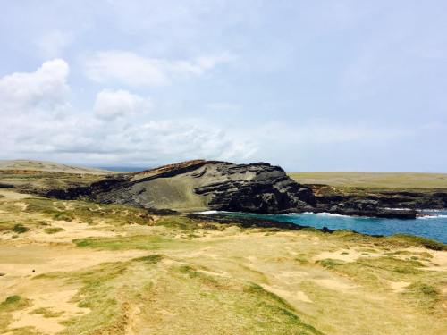 A rocky coastline with green grass and a calm blue sea under a cloudy sky.
