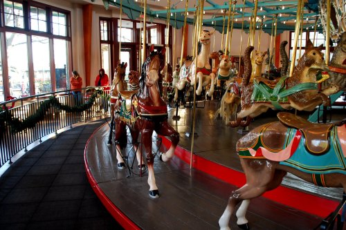 A vintage carousel with colorful horses and animals, surrounded by festive decorations and people in the background.