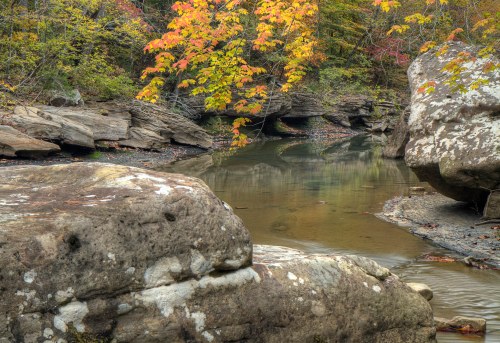 A serene river scene with smooth rocks and vibrant autumn foliage reflecting in the calm water.