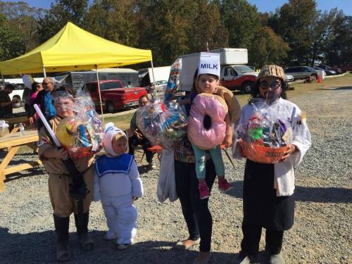A group of children and adults in costumes holding large, colorful baskets at an outdoor event.