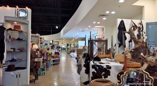 A spacious indoor market with various vendor displays, including furniture, decor, and crafts along a well-lit aisle.