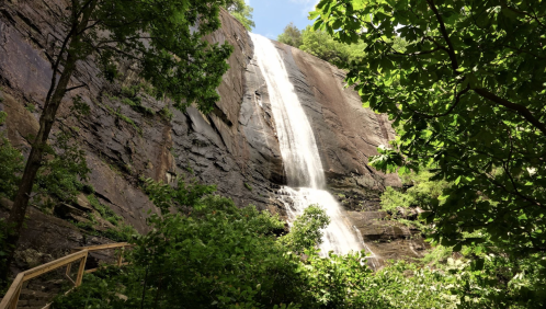 A cascading waterfall flows down a rocky cliff, surrounded by lush green trees and foliage.
