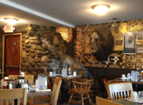 Interior of a rustic restaurant featuring stone walls, wooden tables, and a mounted bison head on the wall.