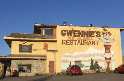 A yellow building with a mural featuring mountains and a totem, labeled "Gwennie's Old Alaska Restaurant."